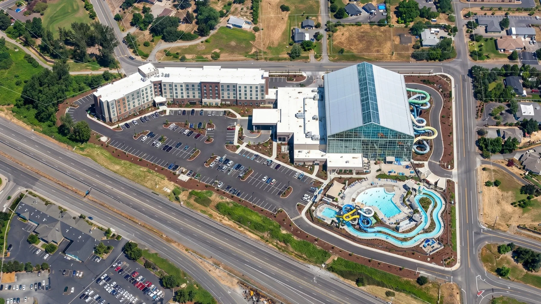 Aerial drone photograph of a hotel, indoor waterpark, pools, and surrounding site